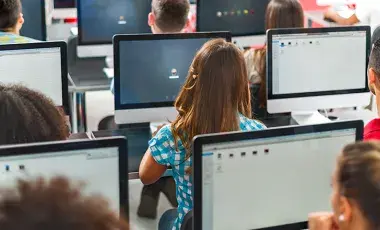 several students sitting at computer in a class room, seen from the back of the room