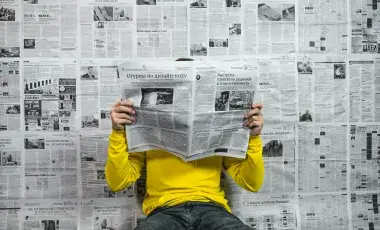 A man sitting on the floor reading a newspaper with newspaper wallpaper in the background