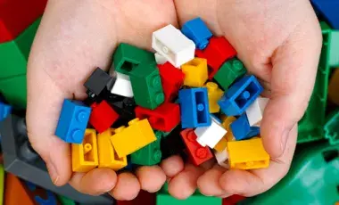 Child’s hands holding a pile of Legos with larger-sized Legos in the background.