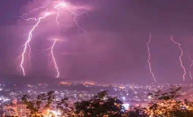 Lightning against a night purple sky over a city landscape