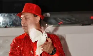 Magician Stoil Stoilov wearing red shirt and hat. Holding a dove and a piece of red cloth