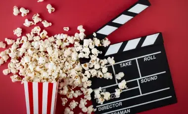 black-and-white film clapperboard and an overturned red-and-white striped box with popcorn spilling out.