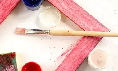 A painted frame with a sponge, paint and paintbrush around the frame.