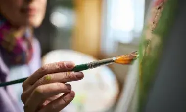 Person holding paint brush and painting on a canvas with paint.