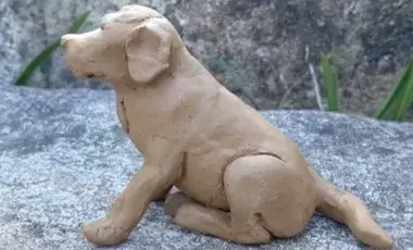 A clay dog facing sideways and sitting on its hind legs