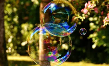 Two large, iridescent soap bubbles floating outdoors in front of a sunny garden background. royalty free photo form pixabay.