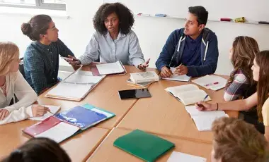 Eight students sit in chairs around a conference table.