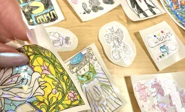 A hand peels an iridescent sticker above a display of other iridescent stickers.