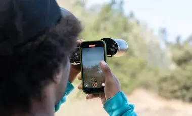 person recording view of nature through binoculars on their smart phone