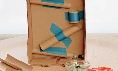 Cardboard rolls taped to a larger cardboard rectangle with a bowl of marbles in front 