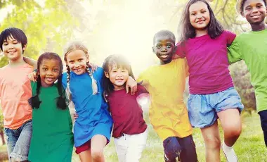 Six children in a row, smiling, wearing colorful shirts, with trees in the background.