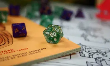 Twenty sided dice centered with many other dice scattered around it, all on top of a map/game rulebook