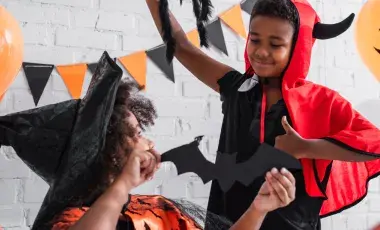 A child dressed as a witch and a child dressed as a devil hang Halloween decorations.