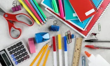 A collection of brightly colored school supplies, like notebooks, scissors, pencils, markers, a ruler, glue, pens, an eraser, and a calculator.
