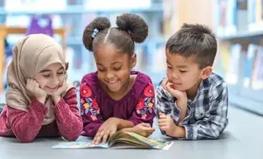 Three kids reading a book together on the floor.