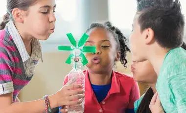 Children blowing on a pinwheel attached to  water bottle