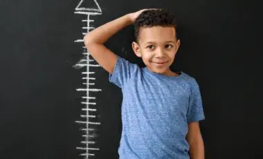 a young boy stands in front of a line of chalk height measurements on a black wall