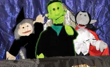 Witch, monster, and vampire puppets in front of a purple curtain