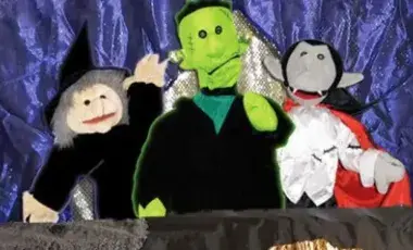 Monster puppets smile in front of sparkly purple background. 