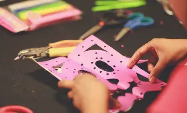 Hands holding tissue paper cut to look like a skull with crafting tools spread around it