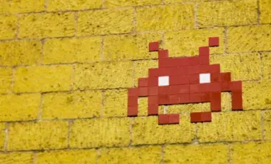 an alien aka "a space invader" created with red tiles on a yellow brick wall