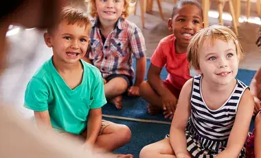 Group of young kids sit on floor rugs listening to a story
