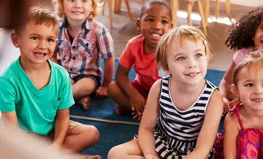 Group of young kids sit on floor rugs listening to a story