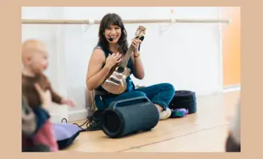 Woman sitting on floor, smiling, and playing ukulele. Baby smiling.