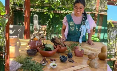 Artist Taty Hernandez stands behind a table of ceramic bowls and vases.