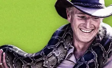 A smiling man in a hat holds a boa constrictor
