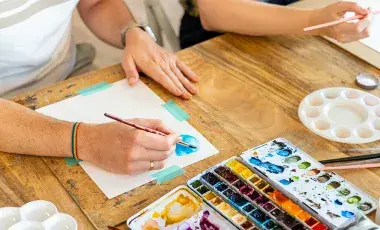 two individuals with watercolor paints at a table