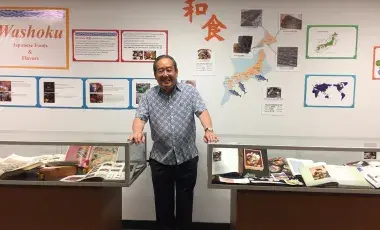Samuel H. Yamashita stands next to glass cases at exhibit with the title, "Washoku: Japanese Foods and Flavors"