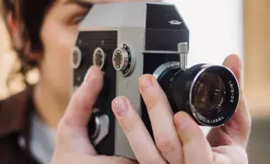 Closeup image of a person looking through the viewfinder of a vintage film camera and adjusting the lens.