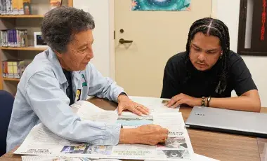 A woman and man sitting at a table reading a newspaper together