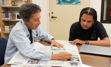A woman and man sitting at a table reading a newspaper together