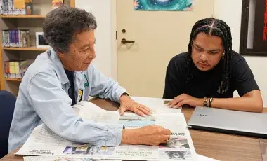 A woman and man sitting at a table reading a newspaper together