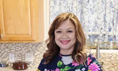 Portrait of author, Alicia Maher, cutting tomatoes on a cutting board in a kitchen
