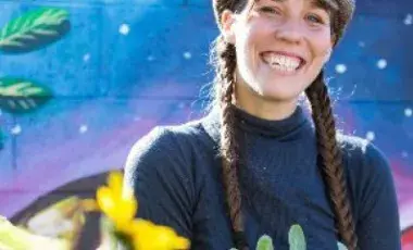 Image of Brie Wakeland with long, brown braids, navy shirt, and a colorful background. 