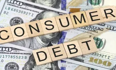 the word "Consumer Debt" spelled with wooden blocks on top of dollars.