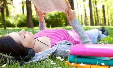 girl reading on grass with headphones 