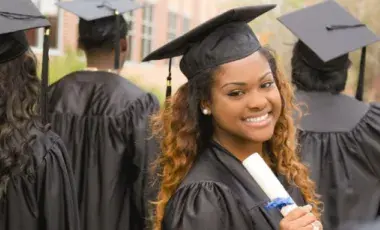 A group of college graduates, three are facing away from the camera and one is facing towards the camera smiling