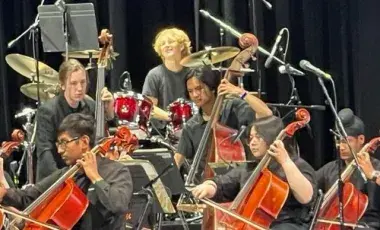Diverse teenagers play cellos and the drums