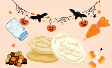 sugar cookies surrounded by Halloween decorations, sprinkles jar, candy, and icing