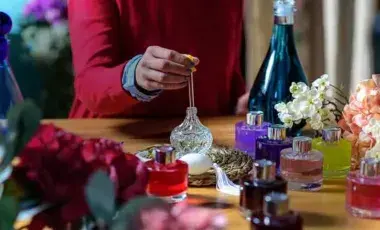 Person at table with perfume making supplies and various perfume bottles and vessels.