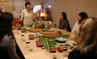 Jessica Wang standing at the head of a table surrounded by 4 adults listening to her instruction.