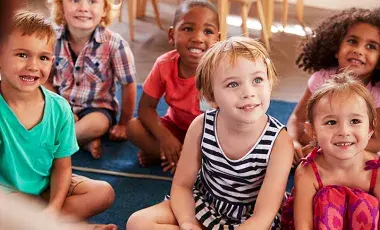 Group of young kids sit on floor rugs listening to a story