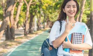 A student smiling on campus with backpacks and notebooks