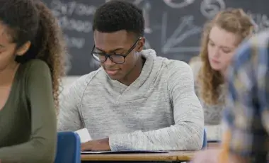 three teens sitting at desks in a classroom filling out test forms