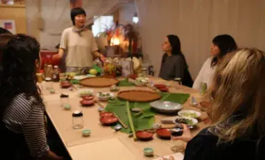 Jessica Wang standing at the end of a table with people around the table. Dishes and small jars are on the table.