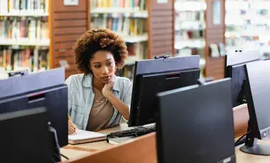 Woman taking notes while looking at a computer